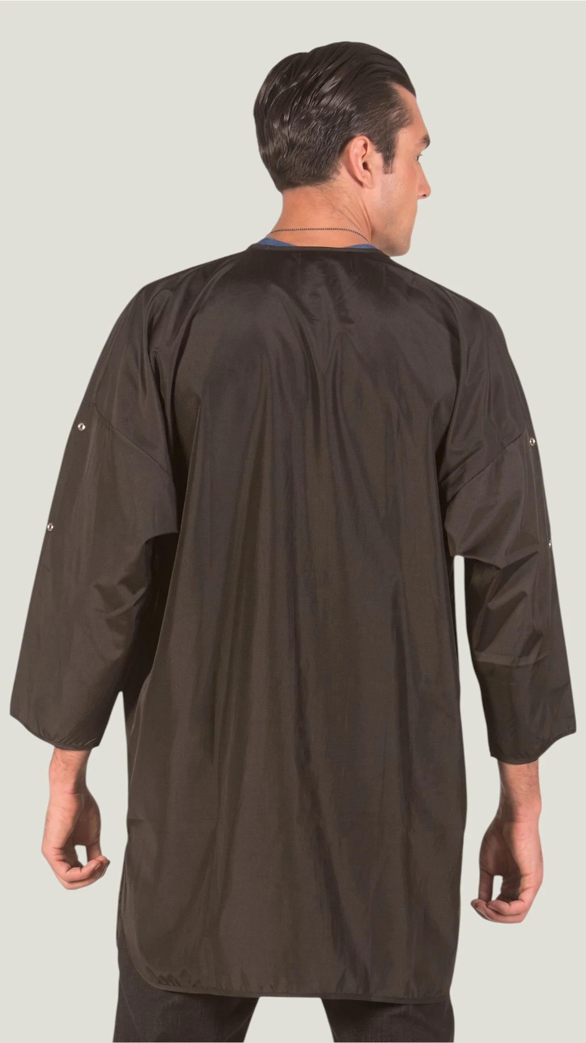 Back view of a dark-haired man modeling the Ladybird Line 428 unisex black water and bleach-resistant groomer and client big shirt smock gown with 3/4 sleeves against a solid light gray background.