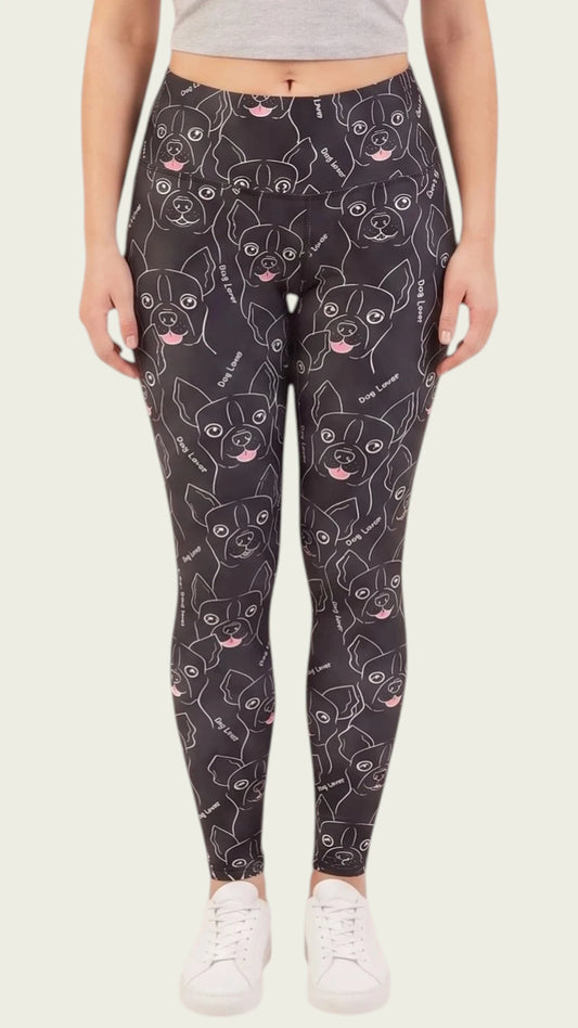 Front view of a woman modeling the Ladybird Line 124 Dog Lover Shadow Hair & Bleach Resistant Grooming Leggings featuring a black dog face line-art print with pink tongue accents, worn with white sneakers against a beige background.