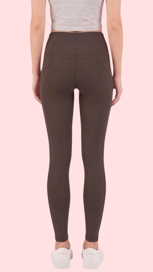 Back view of a woman modeling the Ladybird Line 125 Black Shadow Hair & Bleach Resistant Grooming Leggings, paired with a gray cropped tank top and white sneakers against a pale pink background.
