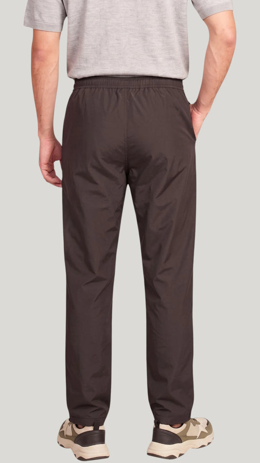 Back view of a man modeling the Ladybird Line 925 Unisex Black Water Resistant & Bleach Resistant Grooming Pants, showing the elastic back waistband, worn with a light grey t-shirt and beige sneakers against a solid light grey background.