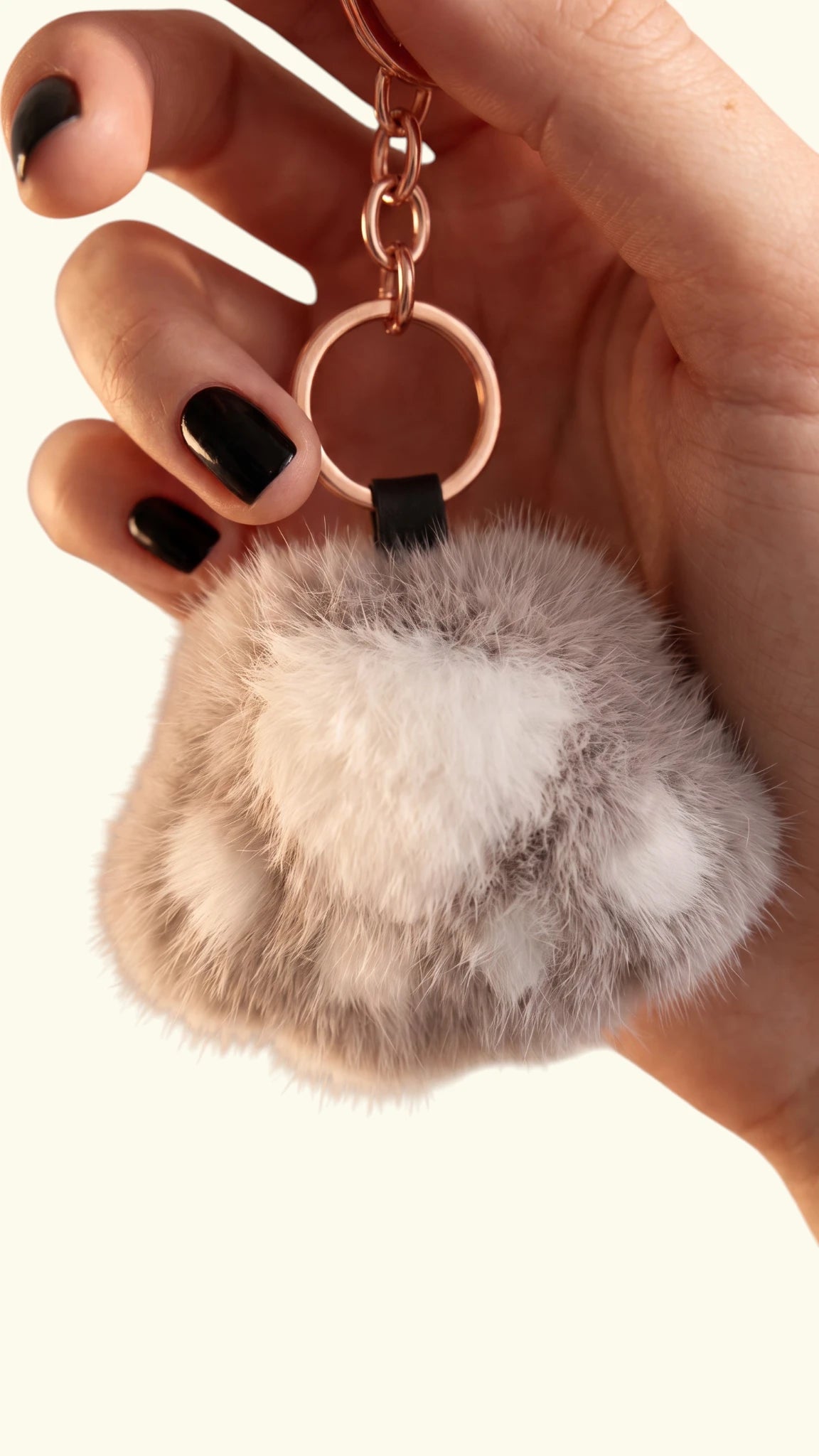 Hand holding a Ladybird Line ash grey and off-white fluffy faux fur dog paw keychain with gold hardware