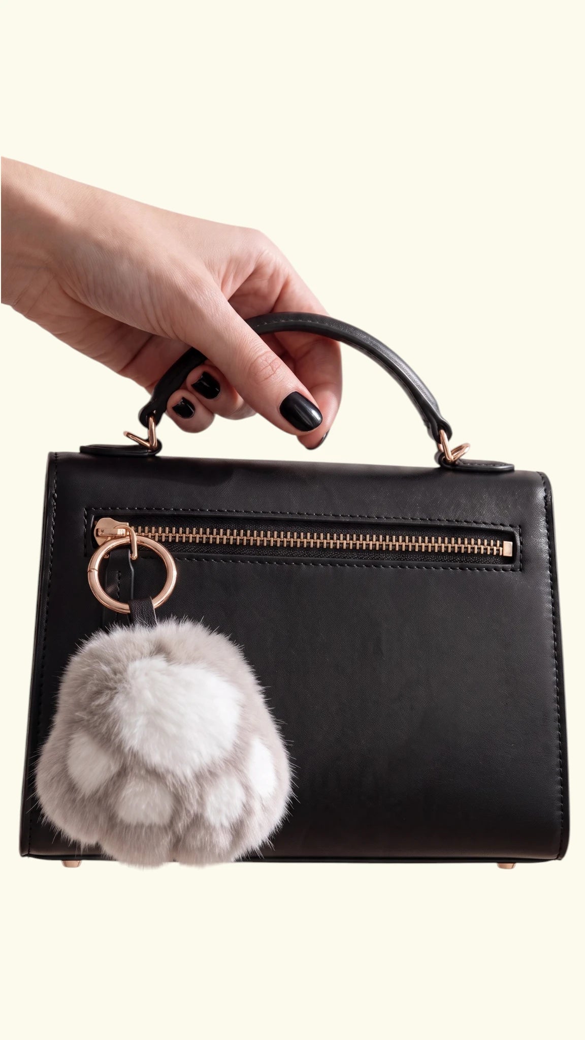 Ladybird Line ash grey and off-white fluffy faux fur dog paw charm clipped to a black leather handbag