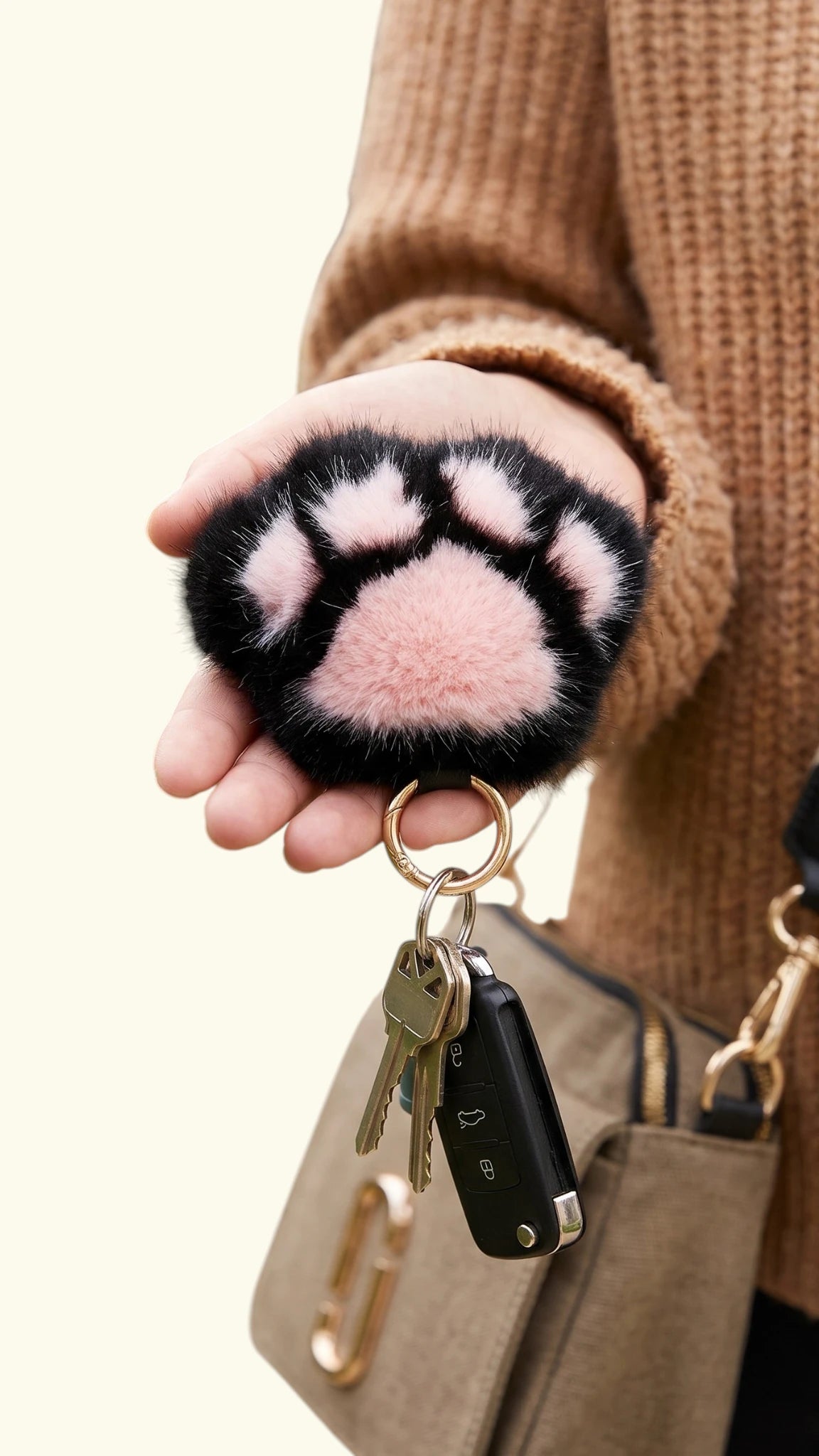 Hand holding a Ladybird Line black and rose pink plush faux fur dog paw keychain with car keys
