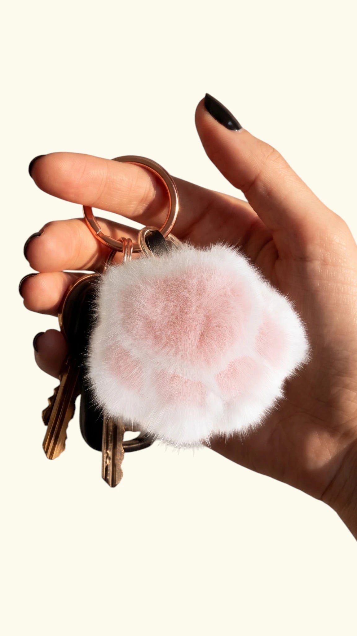 Hand holding a Ladybird Line white and baby pink plush faux fur dog paw keychain with keys