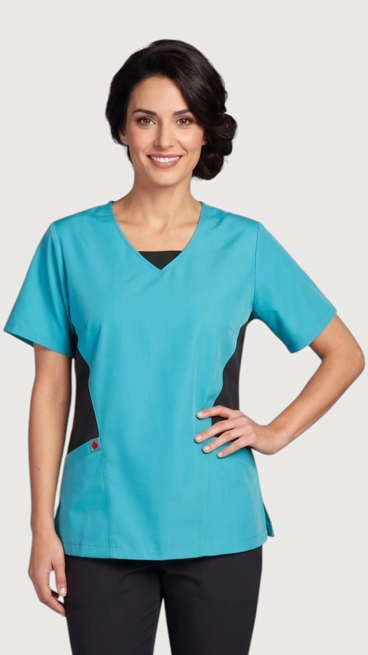 Front view of a smiling brunette woman modeling the Ladybird Line 210 turquoise short-sleeve scrub tunic top with a V-neck, black side panels, and front pocket, paired with black pants against a light grey studio background.