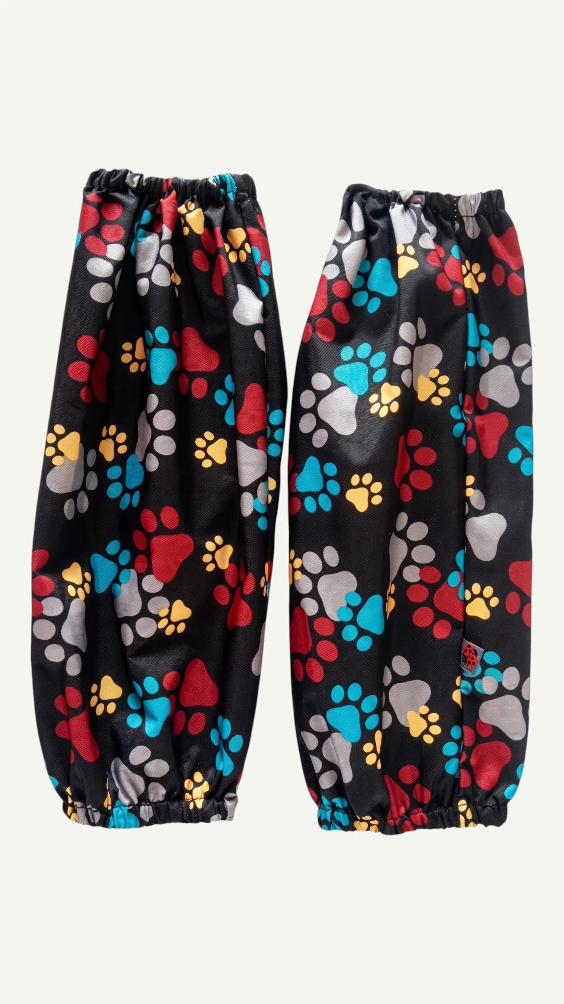 Pair of Ladybird Line 603 waterproof black dog bathing and pet grooming arm sleeves with a colorful red, blue, yellow, and gray paw print pattern and elastic cuffs, displayed flat against a plain light background.