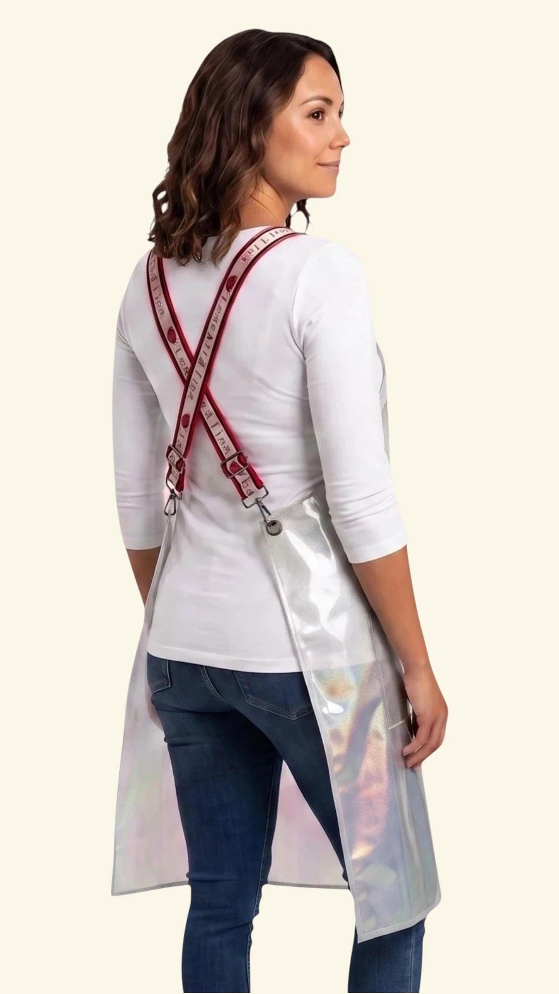 Back view of a young woman modeling the Ladybird Line 111 Waterproof Clear Sparkle Crossover Apron, showing the crisscross red signature straps printed with white 'LADYBIRD LINE' text over a white t-shirt and blue jeans against a light beige background.