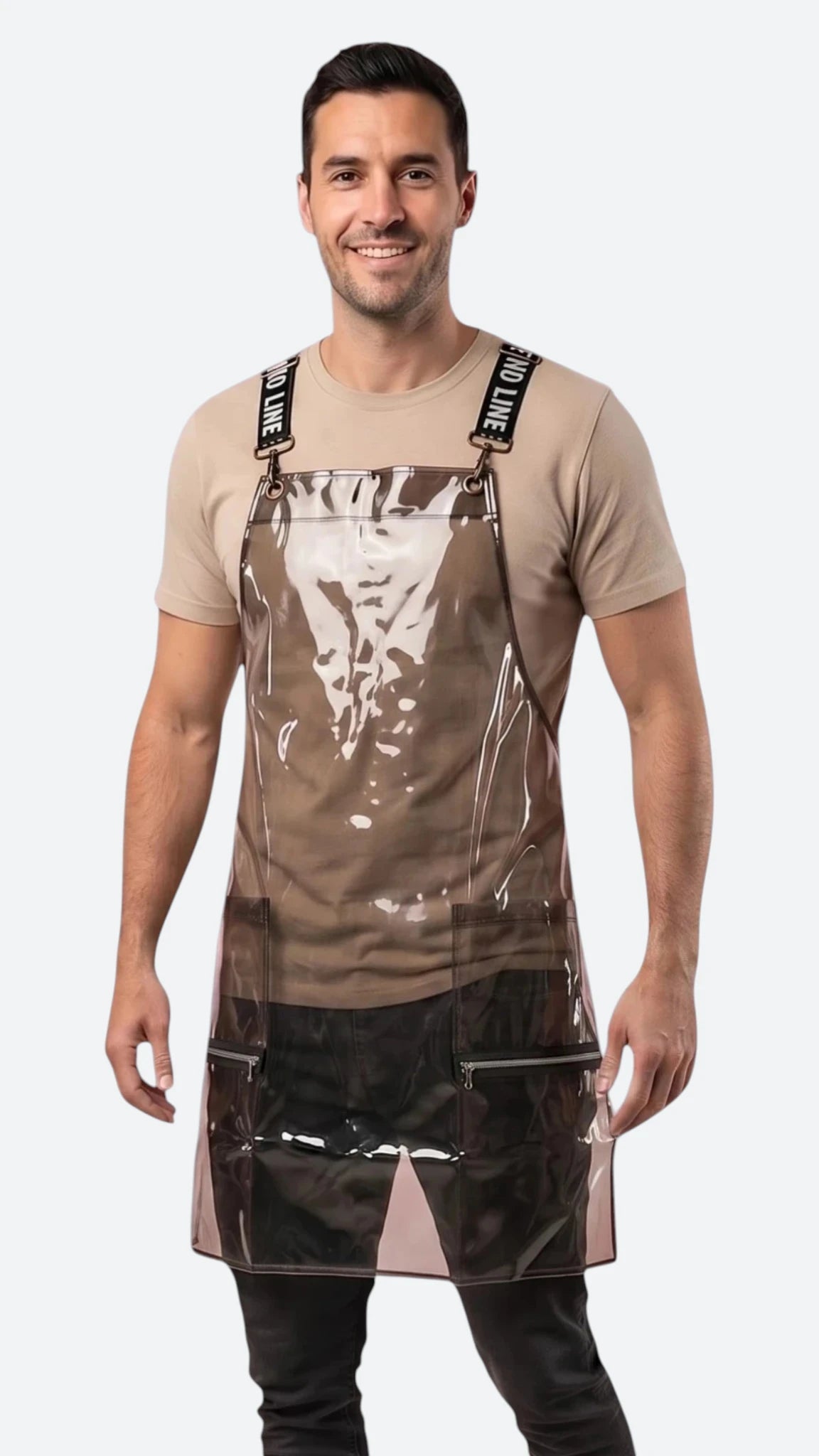 Front view of a dark-haired man smiling while modeling the Ladybird Line 113 Waterproof Black Clear Crossover Apron, featuring a clear waterproof plastic body, black signature crossover straps with white text, and front zippered lapel pockets, worn over a beige t-shirt and dark pants against a solid white background.
