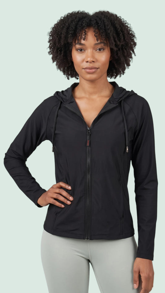 A woman with curly hair modeling the Ladybird Line 122 Black Shadow Hooded Hair & Bleach Resistant Grooming Jacket in a front view with one hand on her hip, worn zipped up over light gray pants against a light green background.