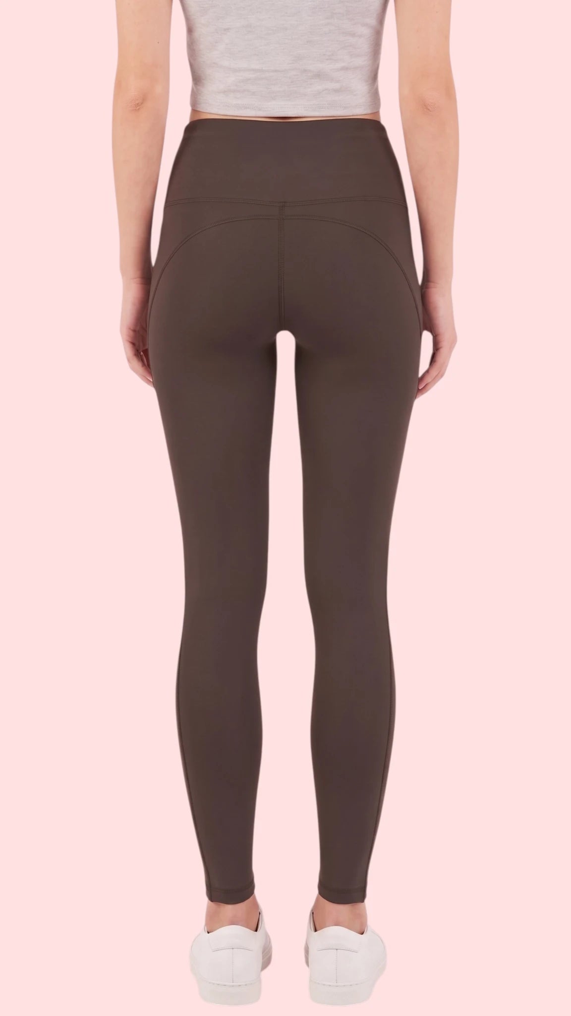 Back view of a woman modeling the Ladybird Line 125 Black Shadow Hair & Bleach Resistant Grooming Leggings, paired with a gray cropped tank top and white sneakers against a pale pink background.