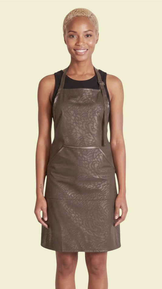 Front view of a woman modeling the Ladybird Line 130 Black Leopard Print Hair & Bleach Resistant Grooming Apron, featuring a subtle black leopard pattern, deep front pocket, and adjustable neck strap, worn over a black top against a pale yellow background.