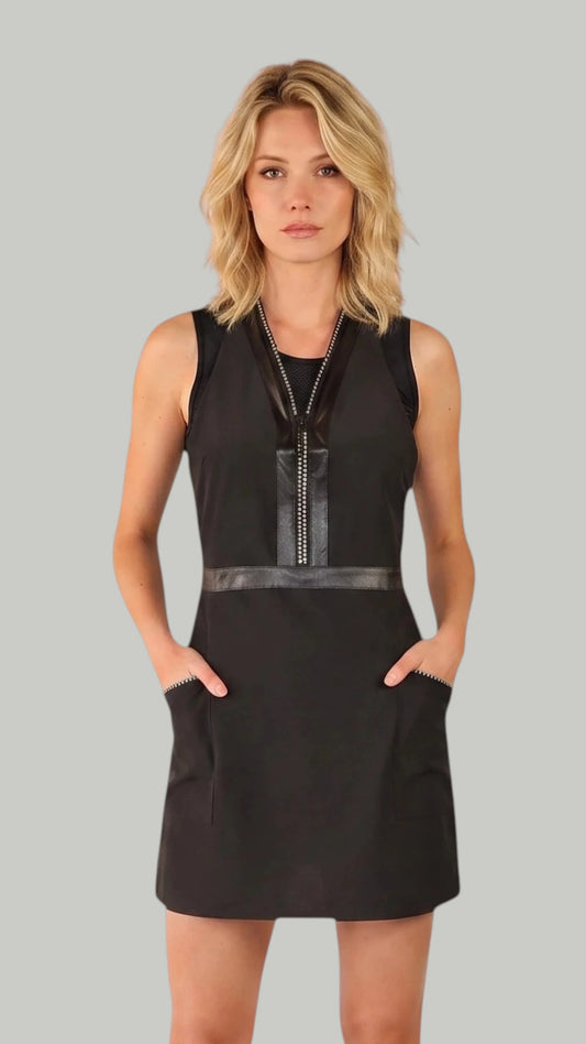 Front view of a blonde woman modeling the Ladybird Line 270 Rhinestone Zipper Water Resistant Styling Apron, featuring a sleeveless black apron dress with a sparkling rhinestone front zipper, faux-leather trim, and deep side pockets, set against a solid light grey background.