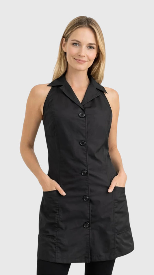 Front view of a smiling blonde woman modeling the Ladybird Line 280 Pro Jacket Style Water Resistant Styling Apron, featuring a black sleeveless vest-style apron with a lapel collar, five decorative front buttons, and deep side pockets, worn over black pants against a solid light grey background.