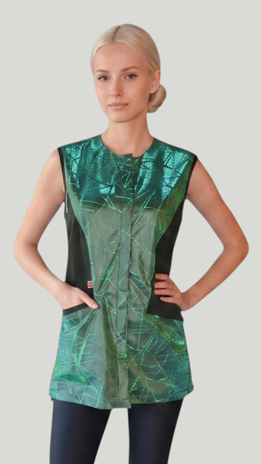 Front view of a blonde woman posing with hands in pockets modeling the Ladybird Line 700 Sparkling Green Waterproof & Bleach Resistant Mesh Back Grooming Vest, featuring a sleeveless grooming vest with a sparkling green color block geometric pattern, covered front zipper, black side panels, and deep pockets, worn over black pants against a light grey background.