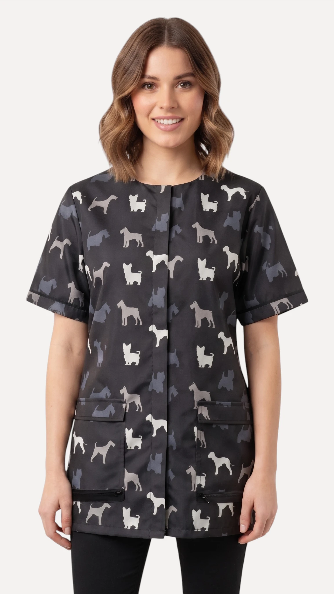 Front view of a dark-haired woman smiling while modeling the Ladybird Line 709 Grey Terrier Unisex Waterproof Grooming Smock, featuring an all-over grey, black, and white dog silhouette print with covered zipper lapels and front pockets, worn over black pants against a solid light grey background.