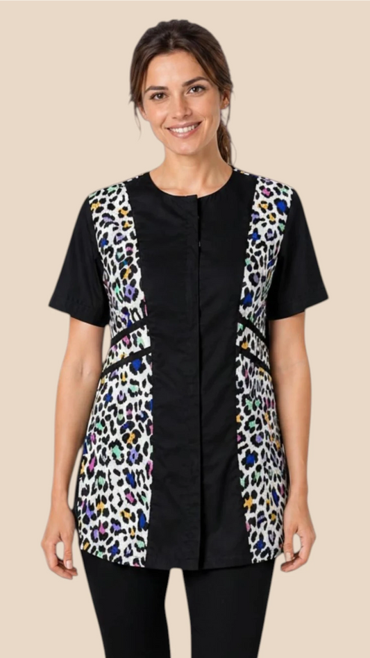 Front view of a dark-haired woman smiling while modeling the Ladybird Line 737 Multi Color Leopard Color Block Waterproof Grooming Smock, featuring a black center panel with vibrant multi-color leopard print side panels, worn over black pants against a solid beige background.