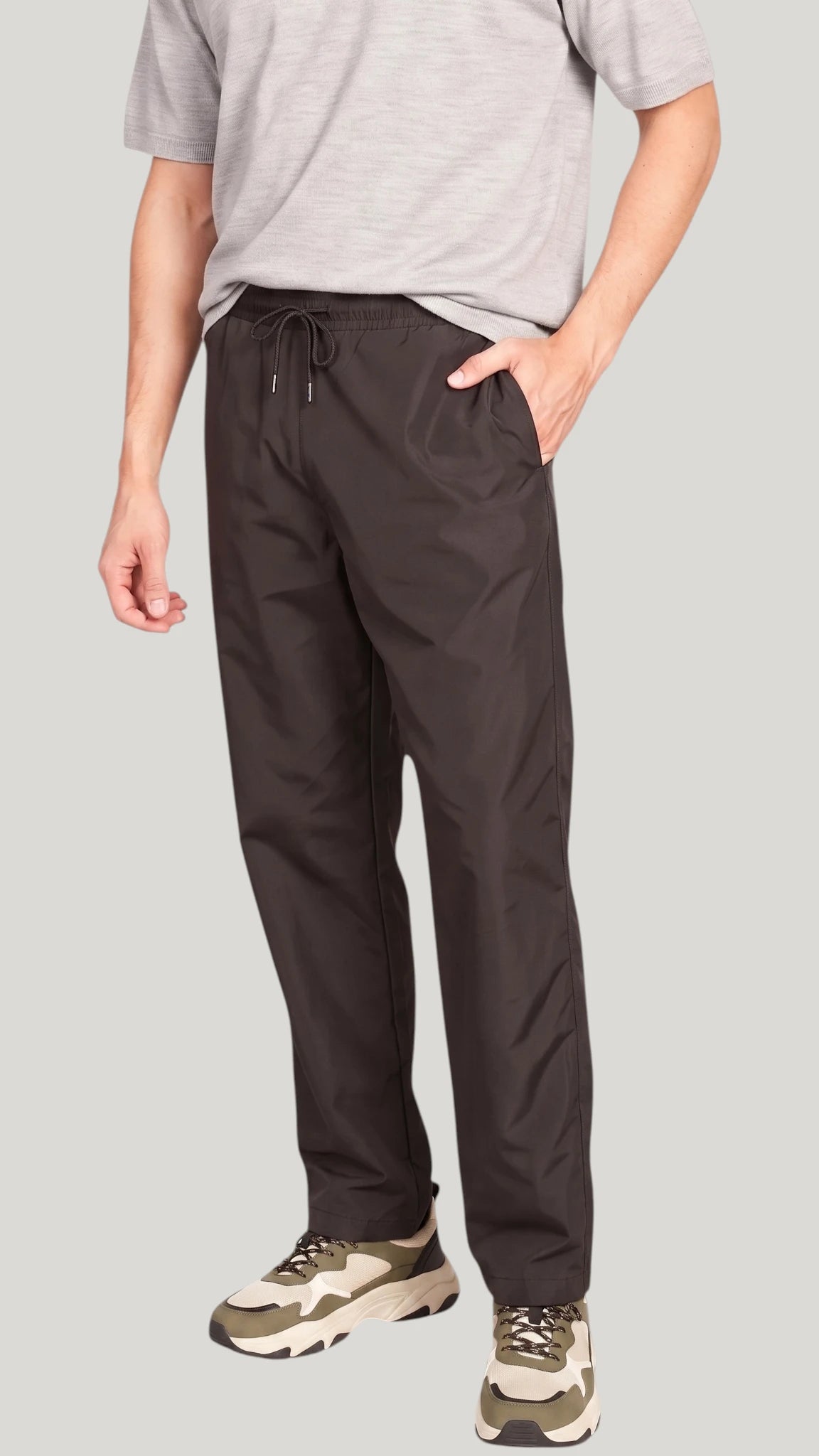 Front view of a man standing with hands in pockets modeling the Ladybird Line 925 Unisex Black Water Resistant & Bleach Resistant Grooming Pants, paired with a light grey t-shirt and beige sneakers against a solid light grey background.