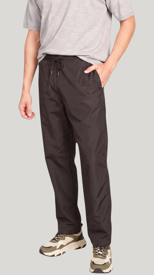 Front view of a man standing with hands in pockets modeling the Ladybird Line 925 Unisex Black Water Resistant & Bleach Resistant Grooming Pants, paired with a light grey t-shirt and beige sneakers against a solid light grey background.