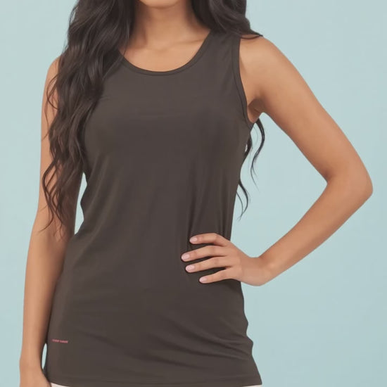 A woman modeling the solid black Ladybird Line 127 Black Shadow Hair & Bleach Resistant Grooming Tank Top in motion, standing with hand on hip paired with light-colored leggings against a light blue background.