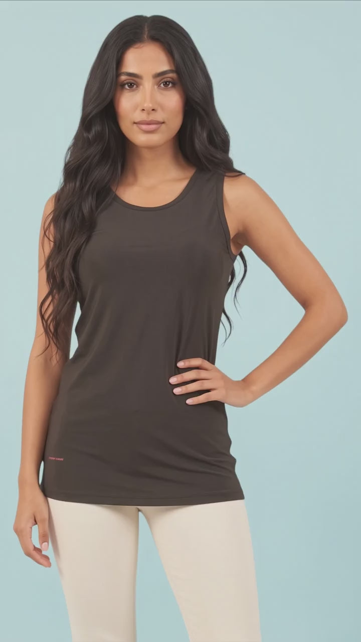 A woman modeling the solid black Ladybird Line 127 Black Shadow Hair & Bleach Resistant Grooming Tank Top in motion, standing with hand on hip paired with light-colored leggings against a light blue background.