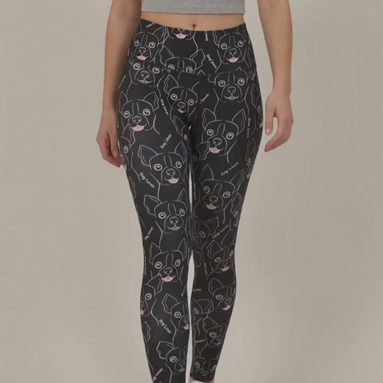 Back view of a woman modeling the Ladybird Line 124 Dog Lover Shadow Hair & Bleach Resistant Grooming Leggings featuring a black dog face line-art print, worn with white sneakers against a beige background.
