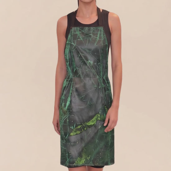 A dark-haired woman modeling the Ladybird Line 142 Green Sparkle Waterproof & Bleach Resistant Apron in motion, swaying side to side over a black top against a pale beige background.
