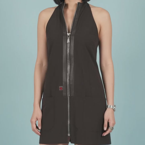 An Asian woman smiling as she models the Ladybird Line 150 Rhinestone Zipper Pro Water Resistant Salon Grooming Apron in black, featuring a center front rhinestone zipper with faux-leather trim, against a solid light blue background.