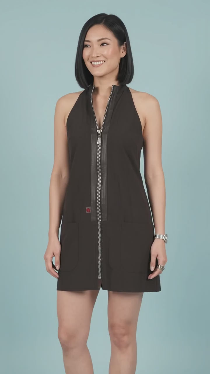 An Asian woman smiling as she models the Ladybird Line 150 Rhinestone Zipper Pro Water Resistant Salon Grooming Apron in black, featuring a center front rhinestone zipper with faux-leather trim, against a solid light blue background.