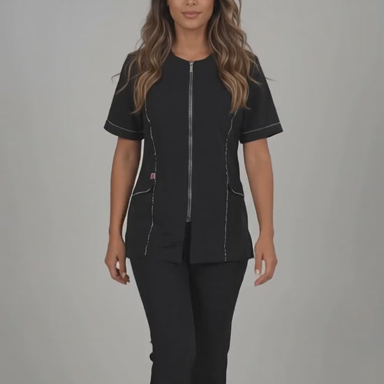A brown-haired woman smiling while modeling the Ladybird Line 850 Rhinestone Trim Water, Bleach & Hair Resistant Styling Jacket, featuring a black short-sleeve styling jacket with sparkling rhinestone trim along the zipper and front lapel, worn with black pants against a solid light grey background.